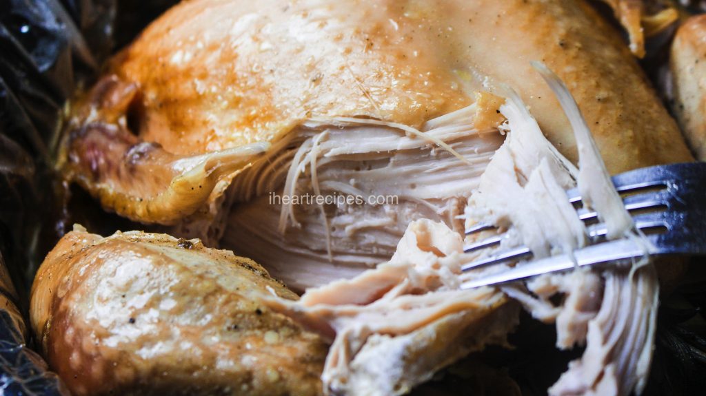 A close-up look at the perfectly tender and juicy turkey breast meat, shredded from the bone with a silver fork. This slow cooker whole turkey is moist and flavorful with golden-brown skin.