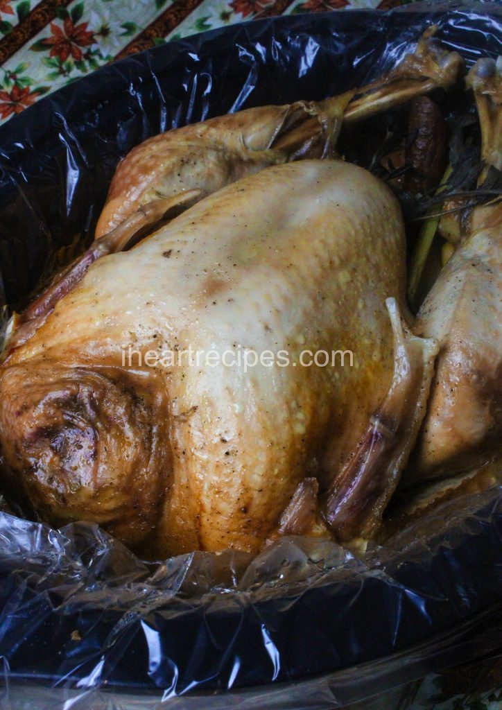 A slow-cooked whole turkey with seasoned golden-brown skin sits in a plastic-lined slow cooker.