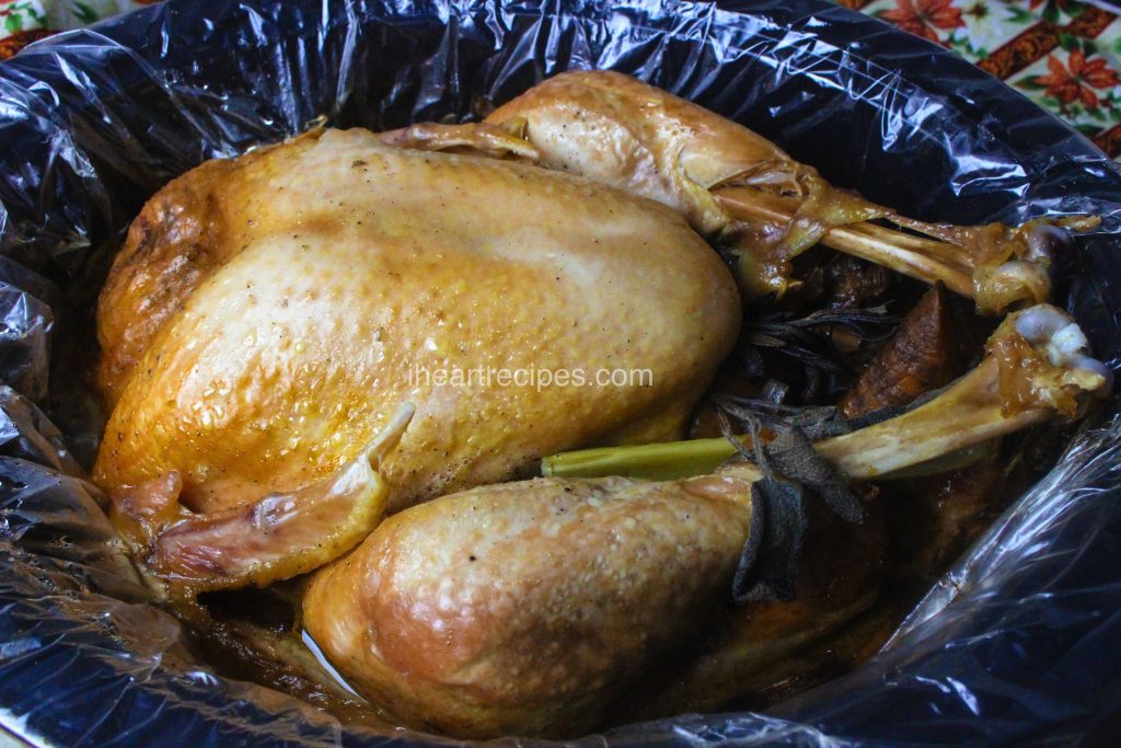 A perfectly slow-cooked turkey with golden-brown skin and turkey leg meat pulling tenderly away from the bone, sitting in a plastic-lined slow cooker pot.