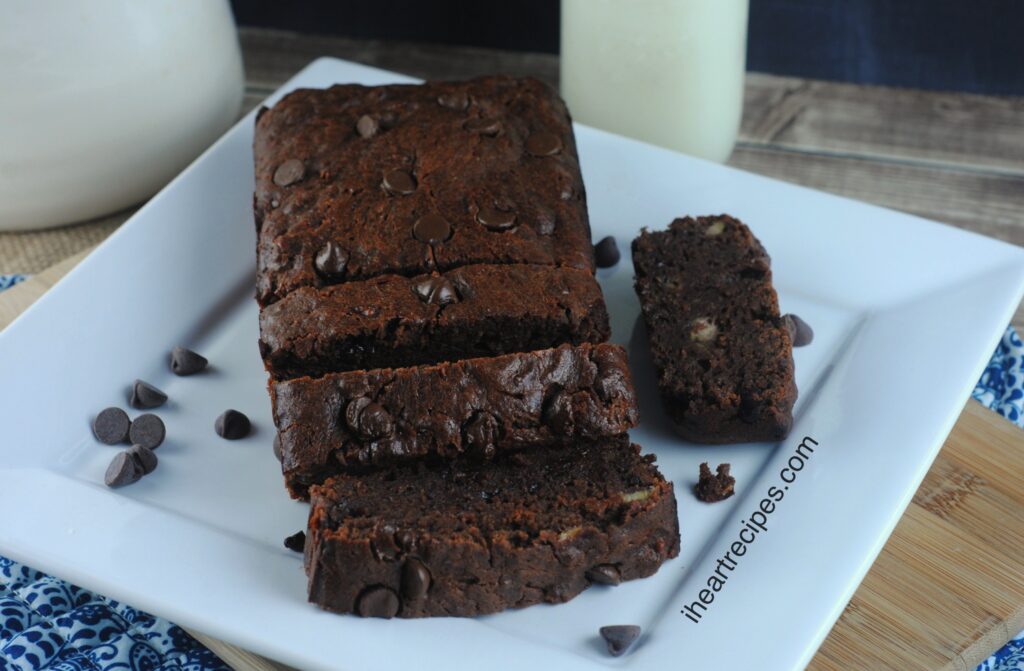 A loaf of Moist Chocolate Banana Bread on a white plate served next to a glass filled with creamy milk. A yummy addition to any brunch buffet!