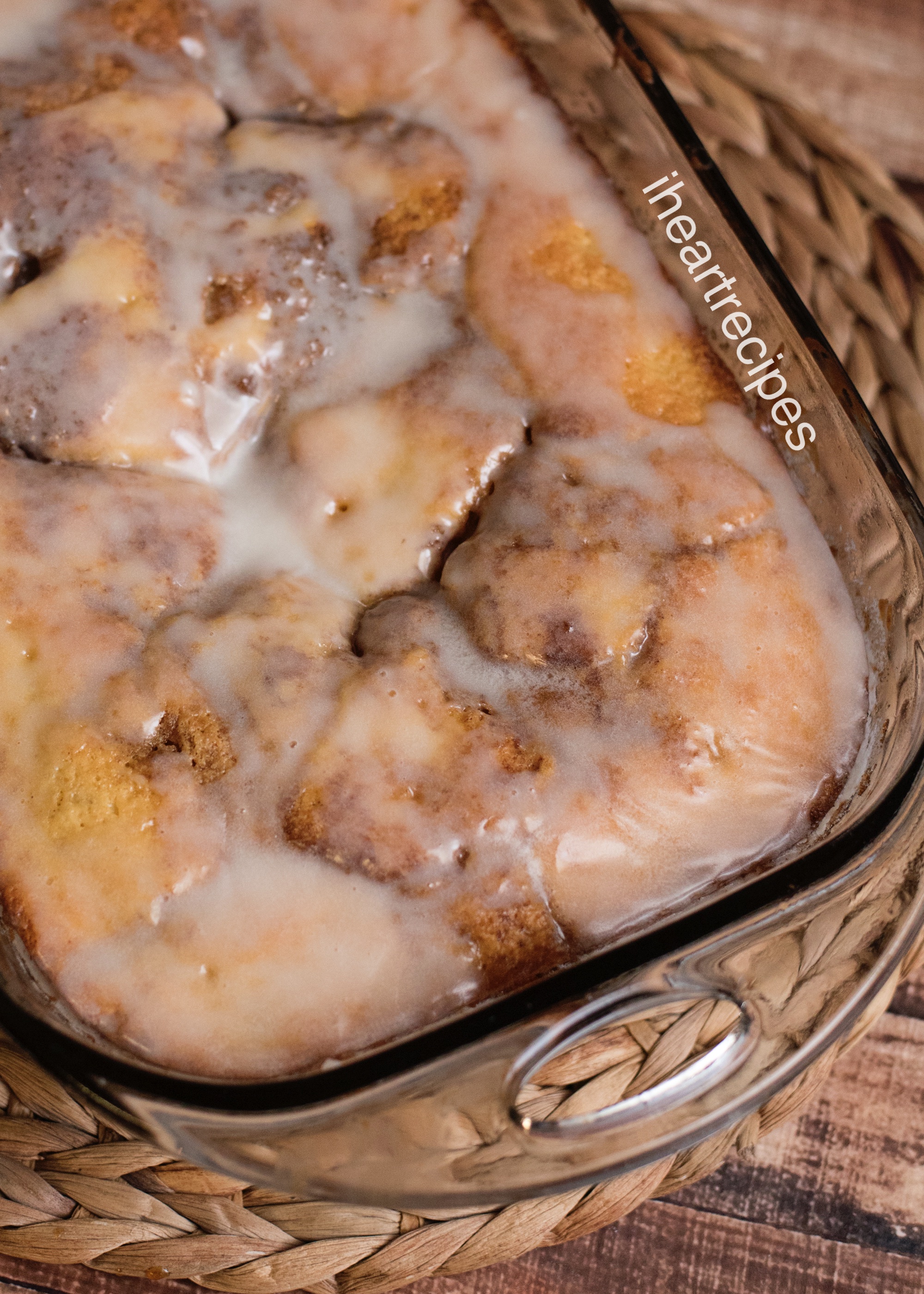 A closeup image of a freshly baked honeybun cake, topped with a sweet vanilla glaze, in a glass casserole dish.