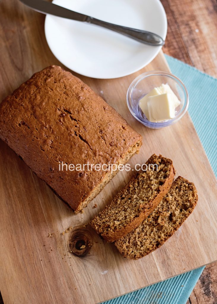 A loaf of moist banana bread sliced and served with soft butter on a wooden cutting board. 