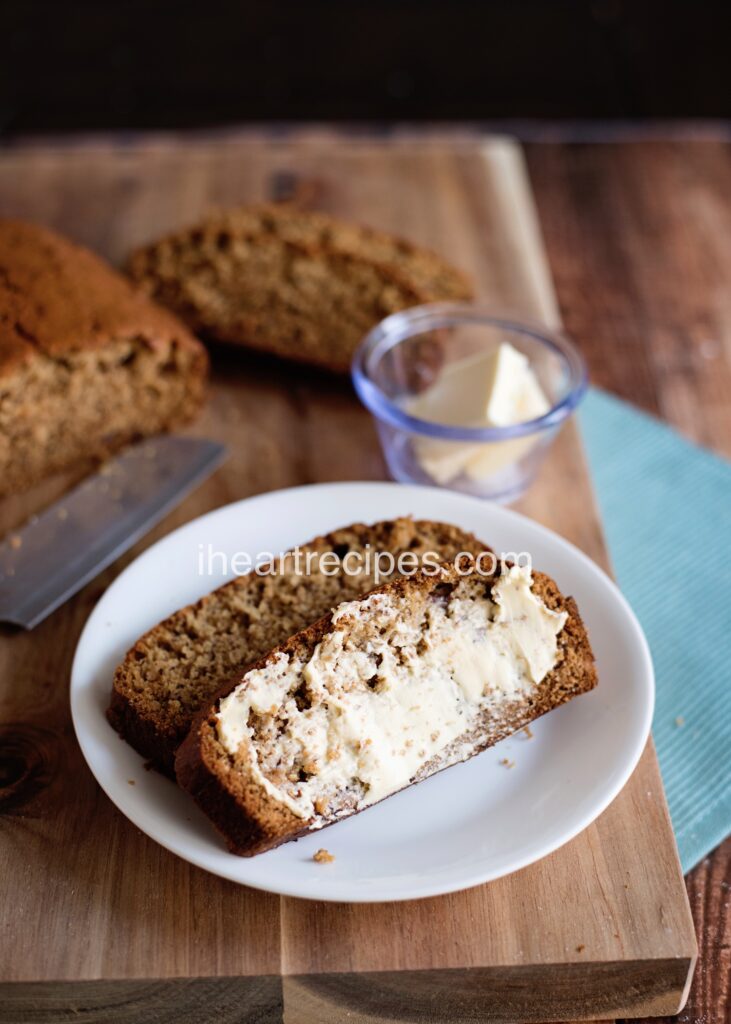 Two slices of delicious banana bread smeared with soft butter served on a white plate. 