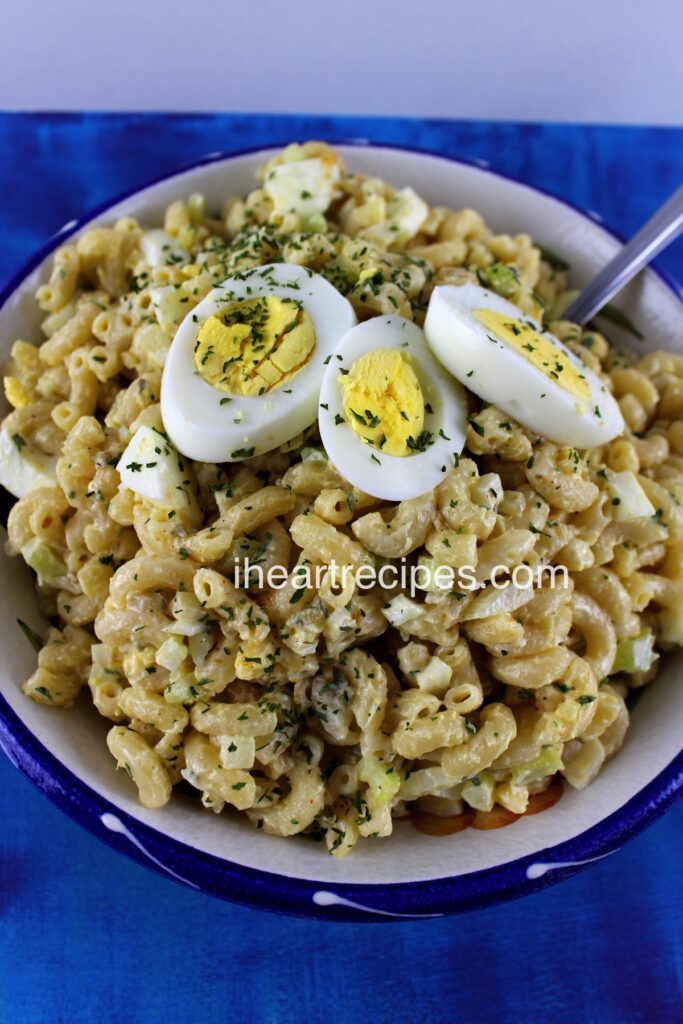 A delicious bowl full of homemade deviled egg macaroni salad, topped with three halved hard-boiled eggs and dried parsley flakes.