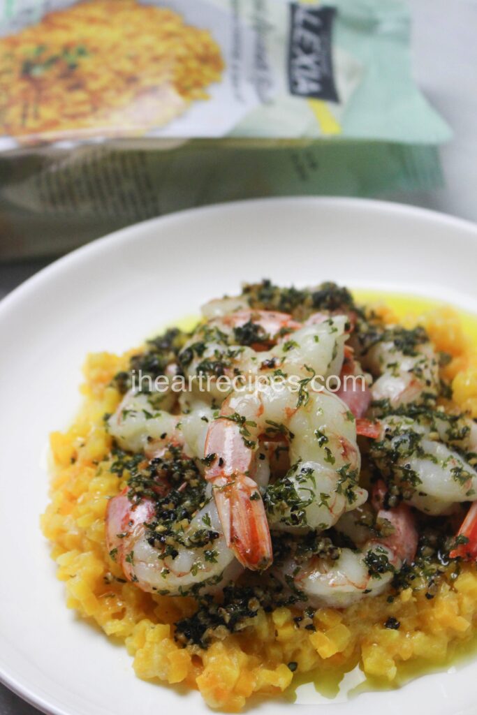 Garlic butter shrimp served on a bed of creamy butternut squash risotto served in a white dish. There is an empty Alexia bag in the background.  