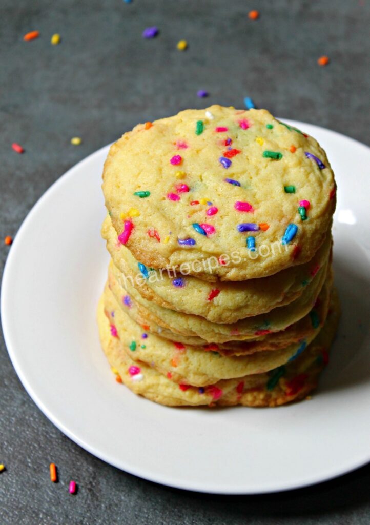 Six cake mix confetti cookies stacked neatly on a round white platter. 