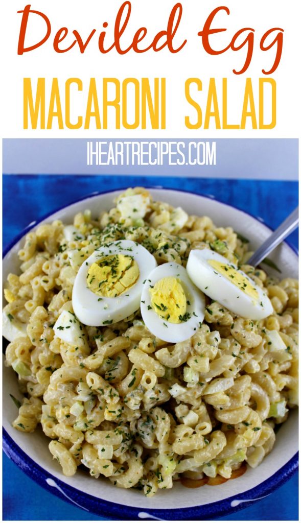 A large bowl filled with fresh-made deviled egg macaroni salad, topped with halved hard-boiled eggs and fresh parsley flakes. Image text reads “deviled egg macaroni salad from iheartrecipes.com” in red, yellow, and white text.