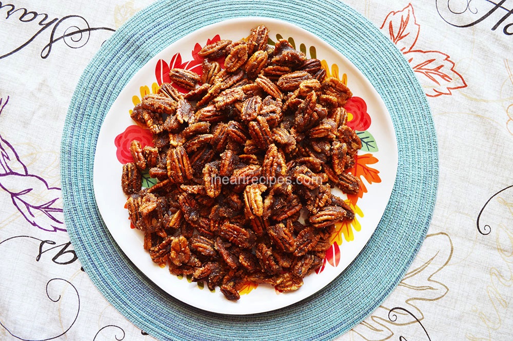 A plateful of crunchy, sweet Candied Pecans set on a light blue placemat and festive fall tablecloth. 