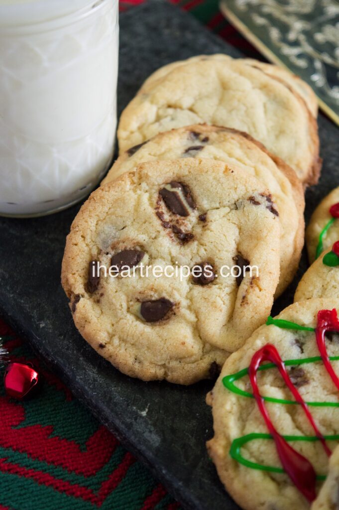 A neat row of cookies with chunks of Andes candy pieces. A glass of milk sits nearby. 