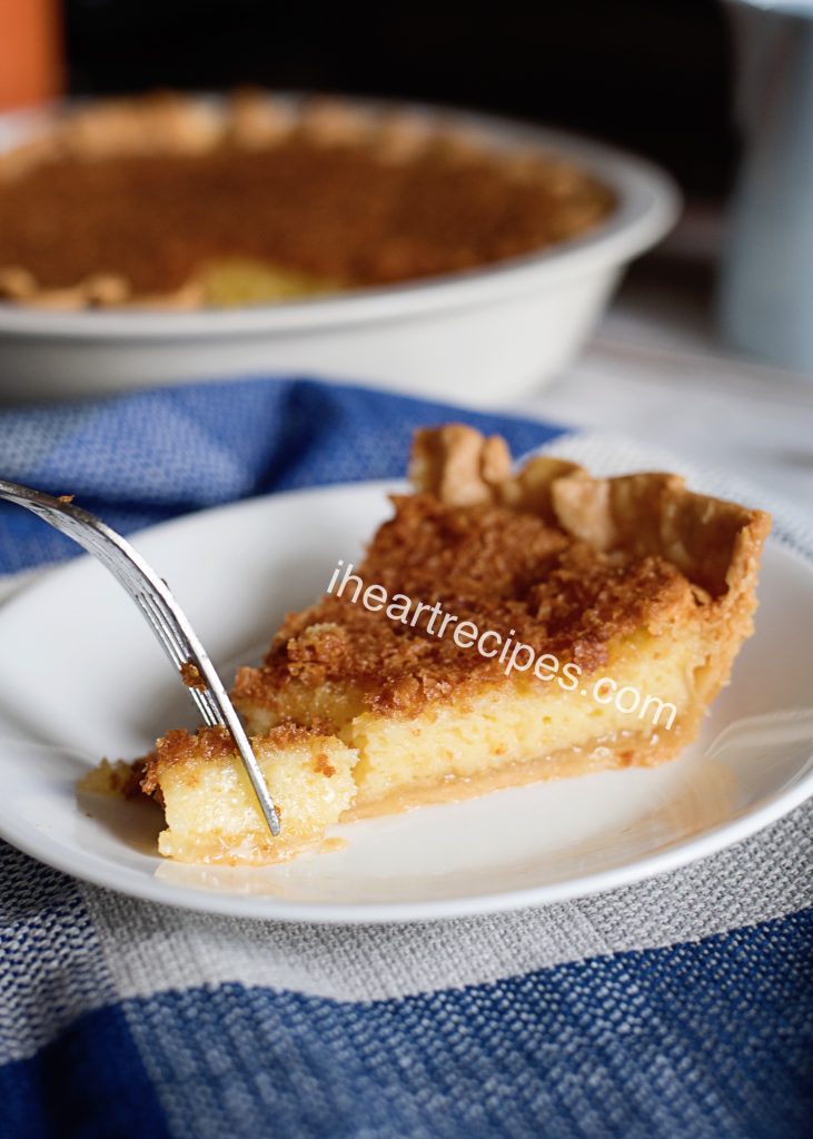 A single slice of old-fashioned chess pie served on a white plate. A silver fork cuts a bite of pie from the end of the piece.