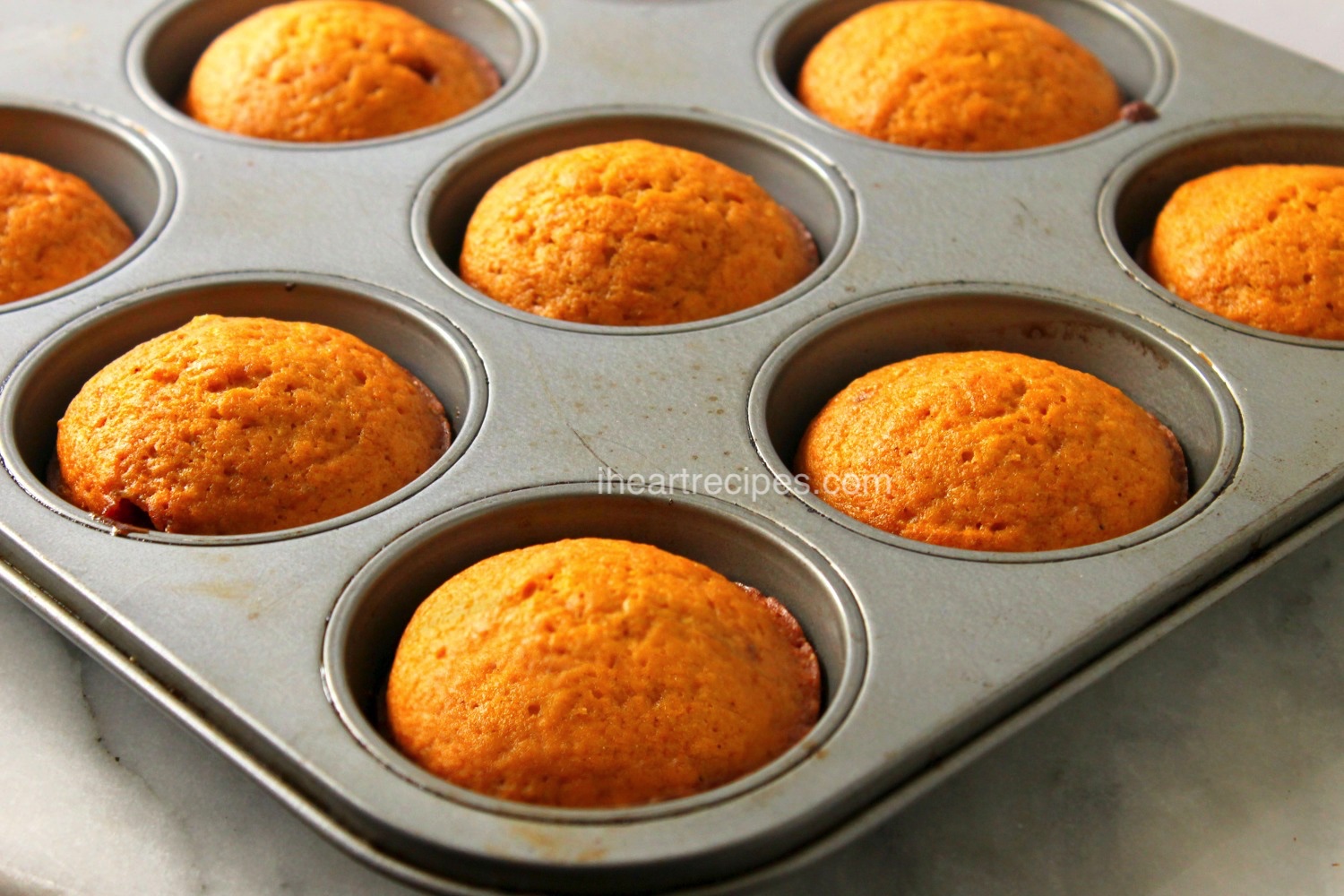 A muffin tin filled with eight homemade sweet potato muffins sits on a marble countertop.