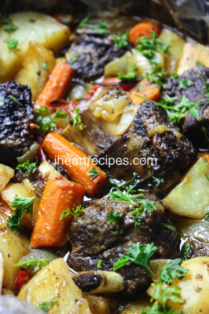 A close-up image of delicious slow cooker short ribs, golden potatoes, tender orange carrots and savory onions garnished with fresh green parsley. 