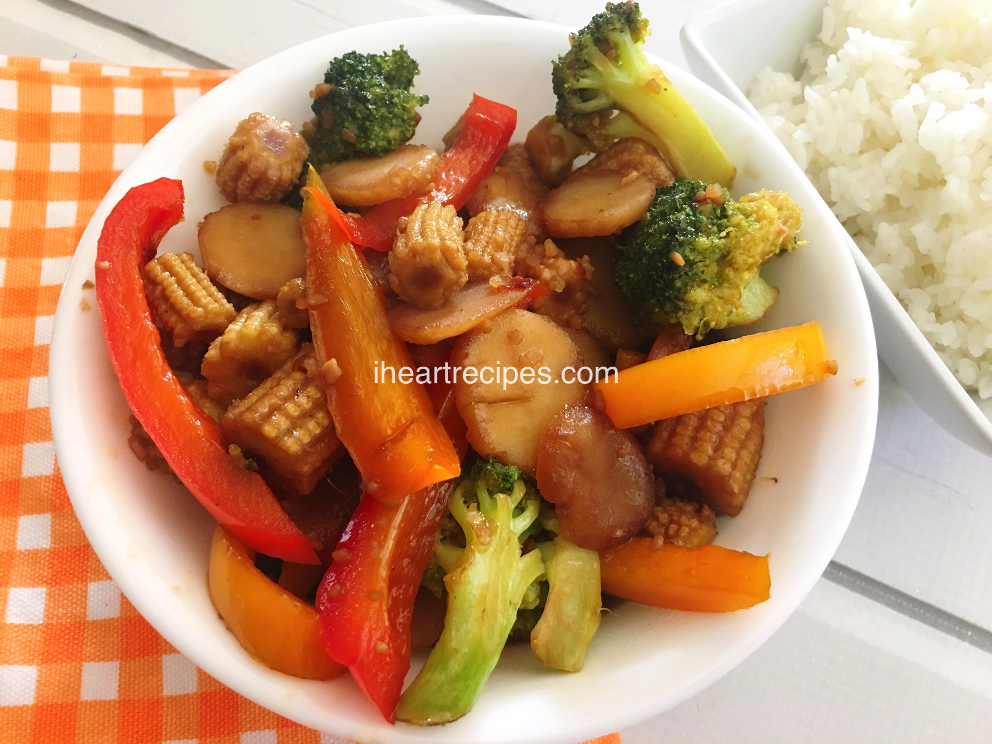 A small bowl of stir fry vegetables -- peppers, baby corns, broccoli, and water chestnuts, cooked in a savory sauce and served with rice.