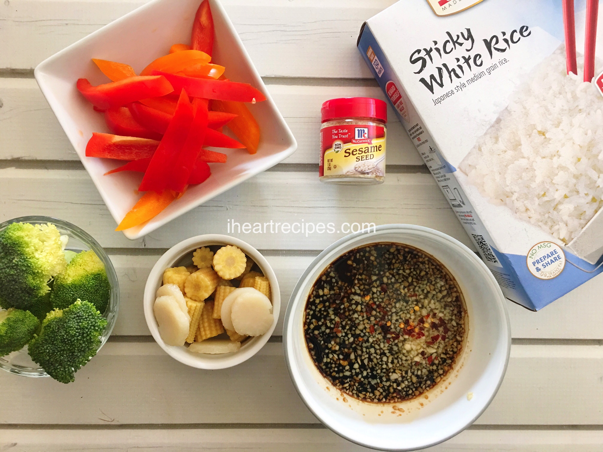 Ingredients needed to make a healthy vegetable stir fry -- sliced bell peppers, broccoli, water chestnuts, baby corns, a simple sauce, sesame seeds, and a box of sticky white rice.