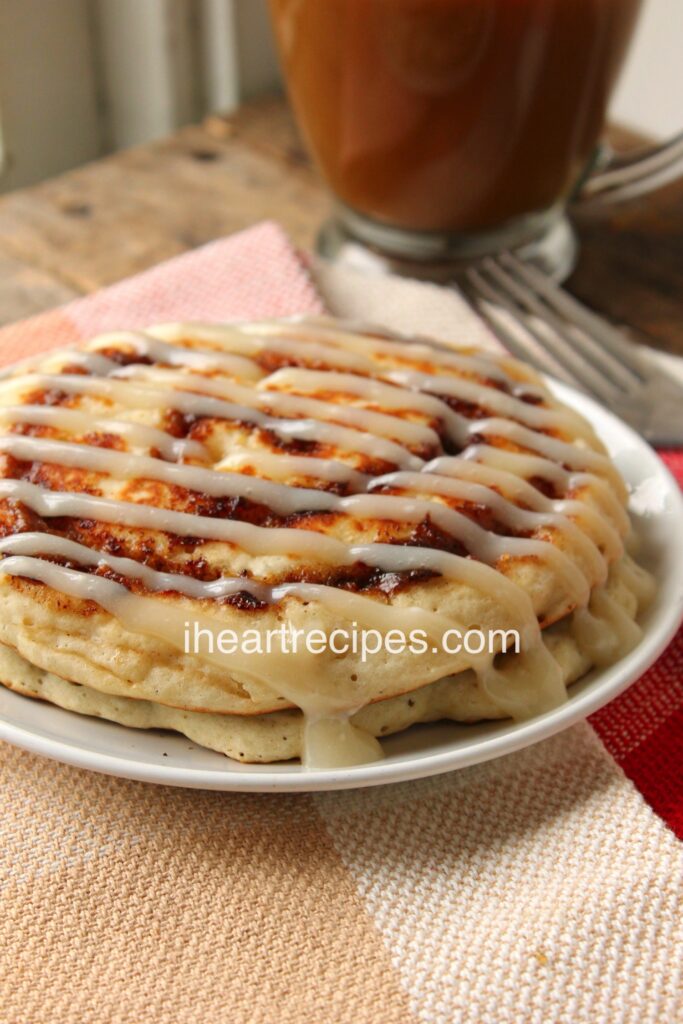 Two homemade cinnamon roll pancakes with cream cheese icing served with a glass of coffee.