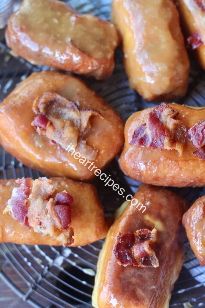 A tray of golden maple donuts topped with pieces of crisp bacon.