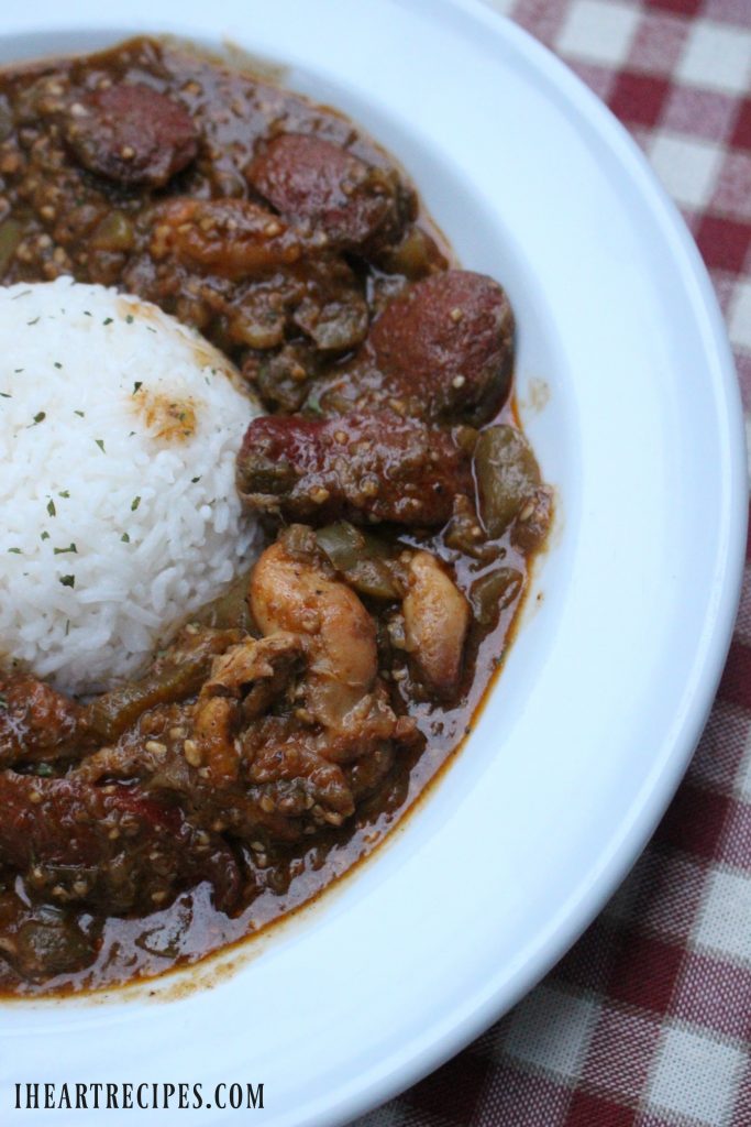 Tender okra and chicken with smoky sausage on a bed of rice served in a white bowl on a red and white checked tablecloth.