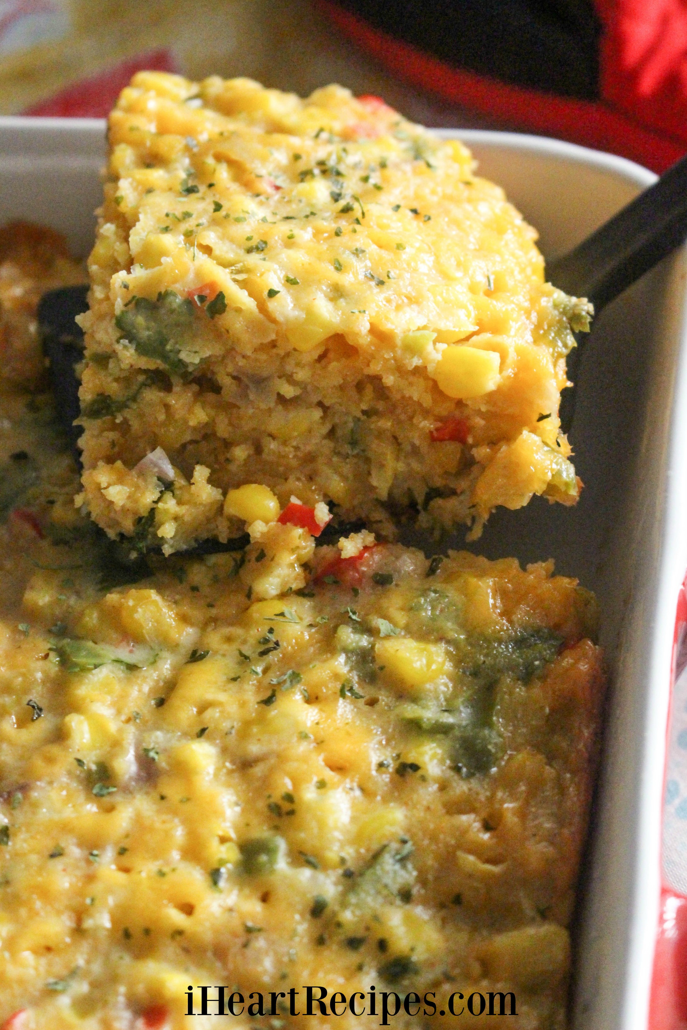 A light and fluffy corn casserole square served from a red baking dish. This casserole is a favorite for any occasion.