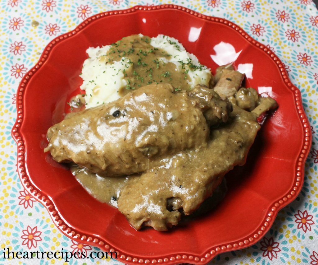 Southern smothered turkey wings and creamy mashed potatoes drenched in gravy served on a scalloped red plate.