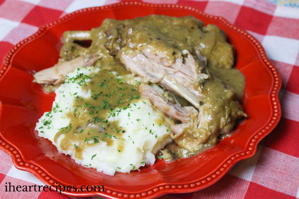 Tender turkey wings, creamy mashed potatoes, and savory gravy on a scalloped red plate.