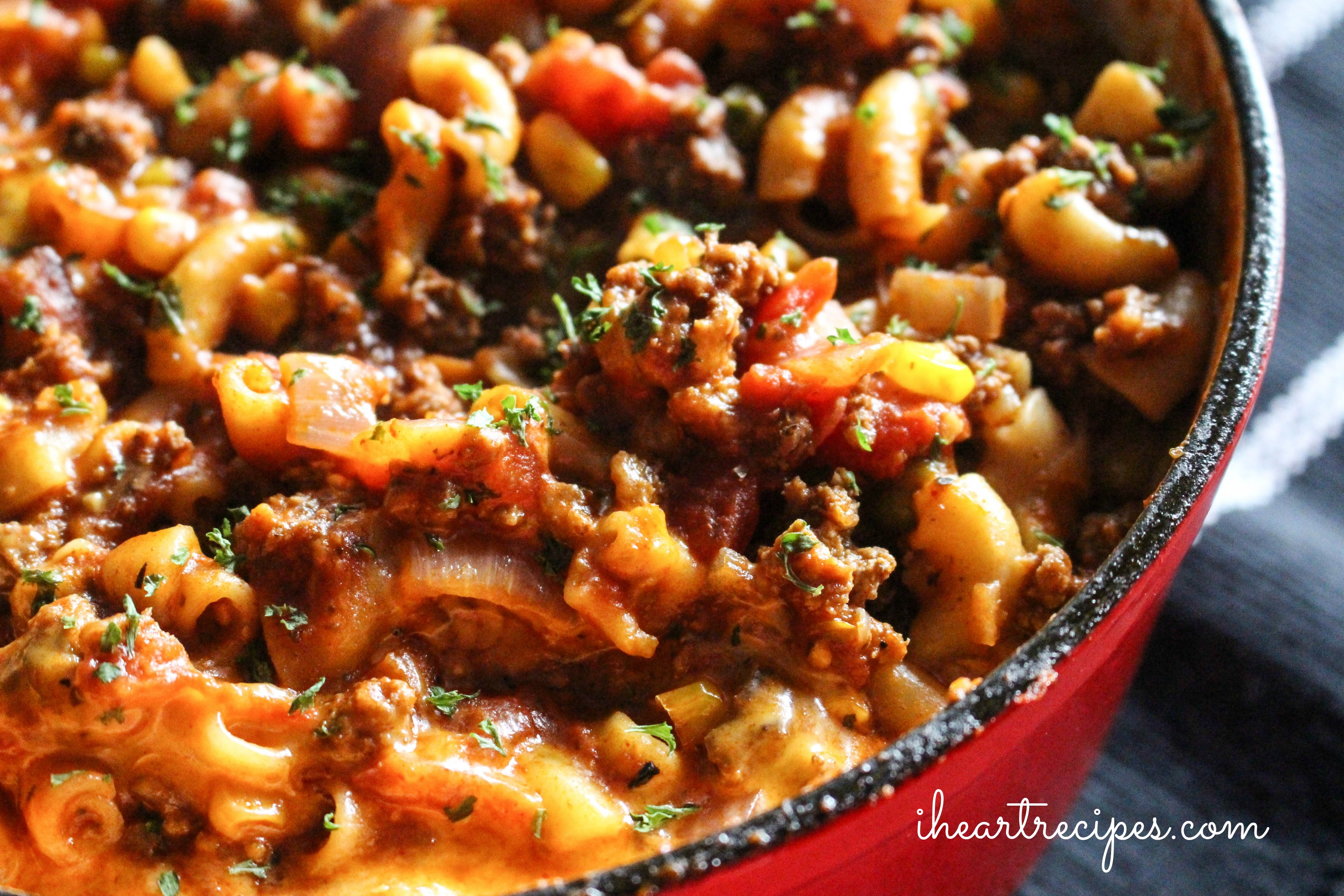 A flavorful Old-fashioned beef goulash garnished with herbs simmering in a red skillet. Enjoy this classic recipe tonight!