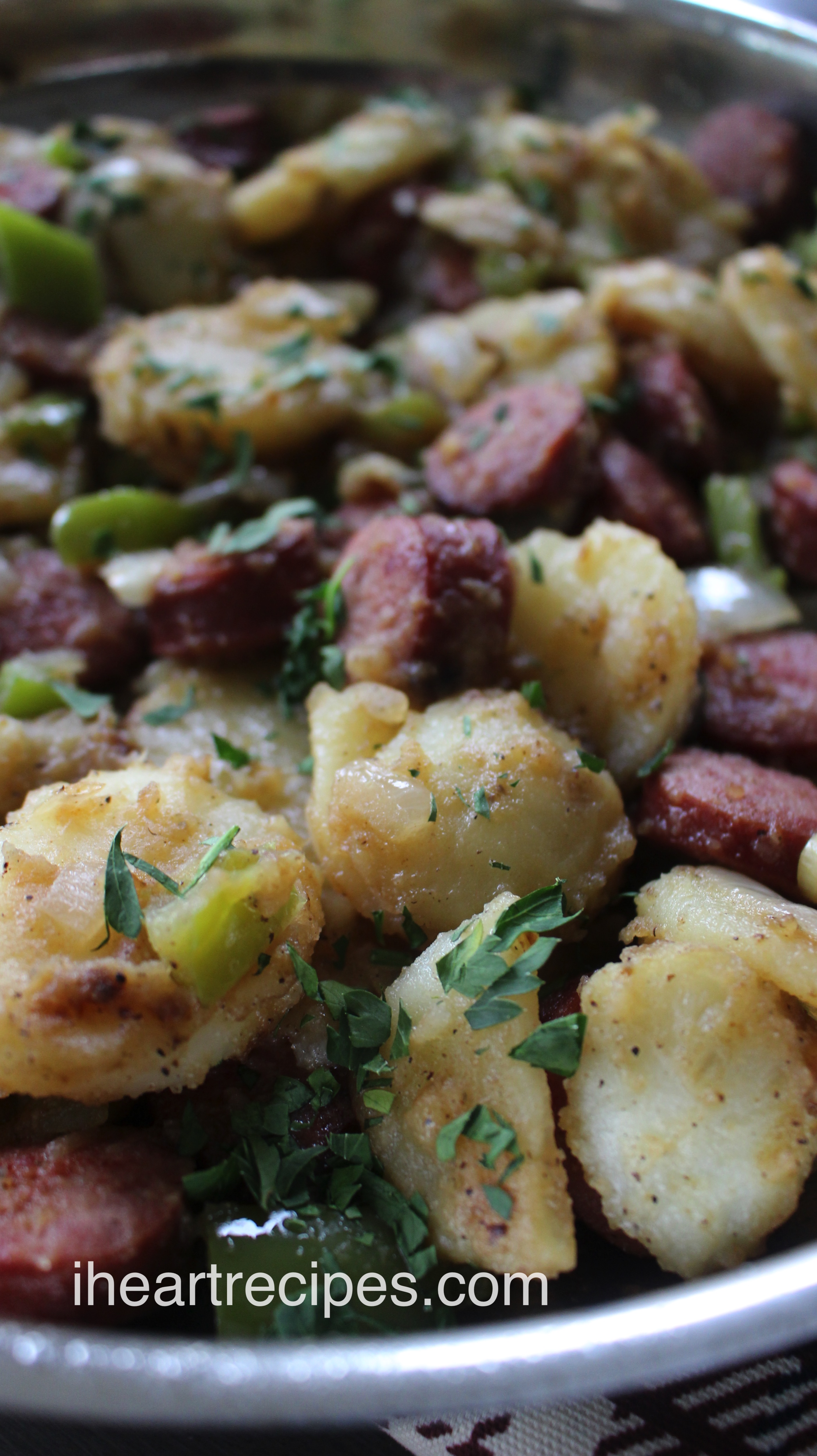 A zoomed-in photo of smothered potatoes and sausage with onions and peppers, cooked until tender in a skillet on the stovetop.