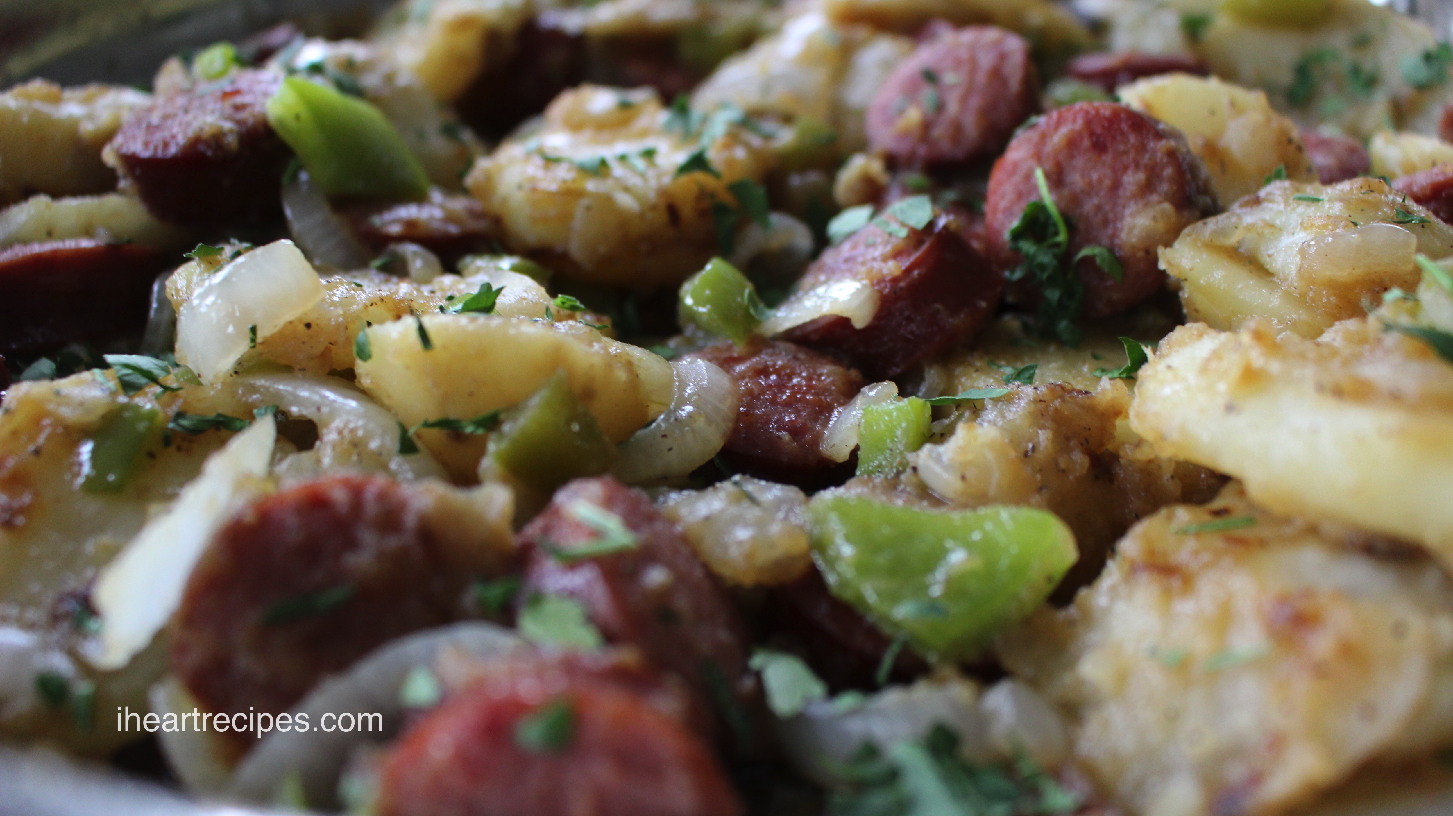 A closeup image of smothered potatoes and sausage cooked with onions and peppers and garnished with fresh herbs for serving.