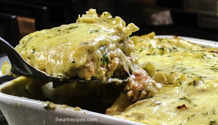 A slice of creamy seafood lasagna is lifted from a casserole dish with a spatula. Seafood is baked between layers of tender lasagna noodles and a creamy white sauce.