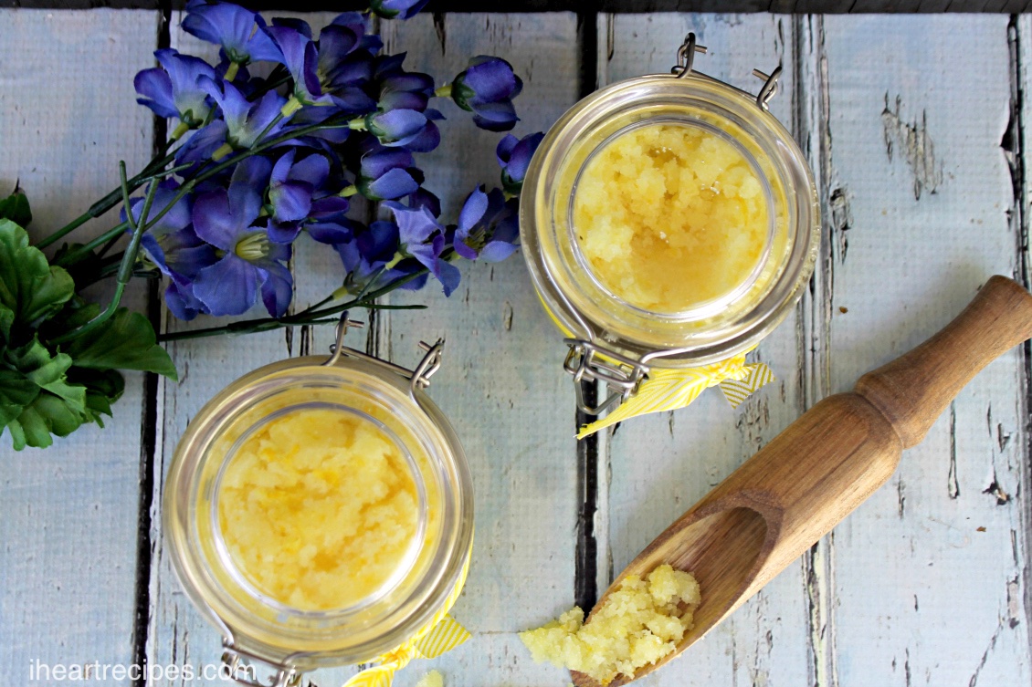 Fragrant, bright yellow, natural lemon body scrub in glass jars sitting atop a rustic wooden table. This scrub is the perfect self care spa day treat!