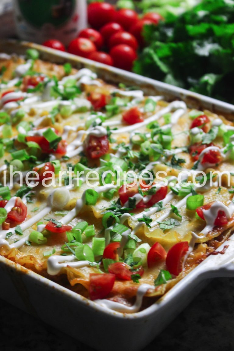 A fresh-made dish of ground turkey taco lasagna casserole, topped with green onions, tomatoes, cilantro, melty cheese, and Mexican crema. 
