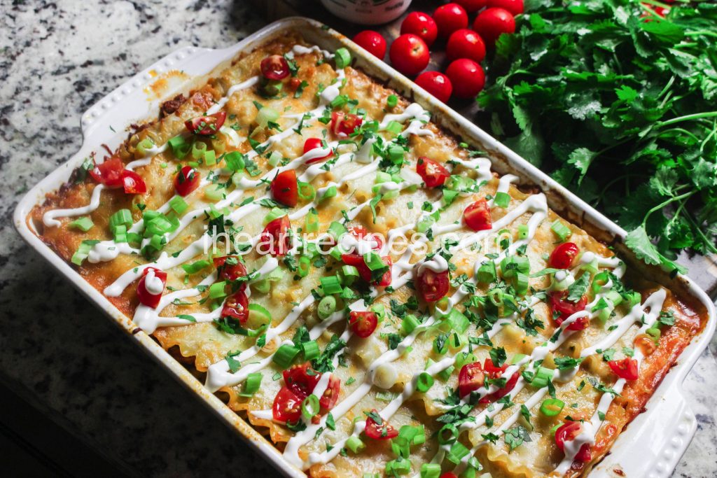 A pan of baked taco lasagna – ground turkey, lasagna noodles, and cheese, layered and topped with sour cream, diced tomatoes, green onions, and cilantro.