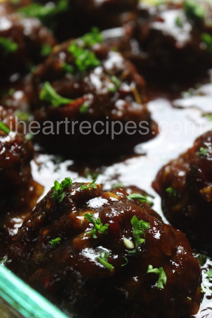 A close up of a meatloaf meatball smothered in a rich sauce and garnished with fresh parsley.