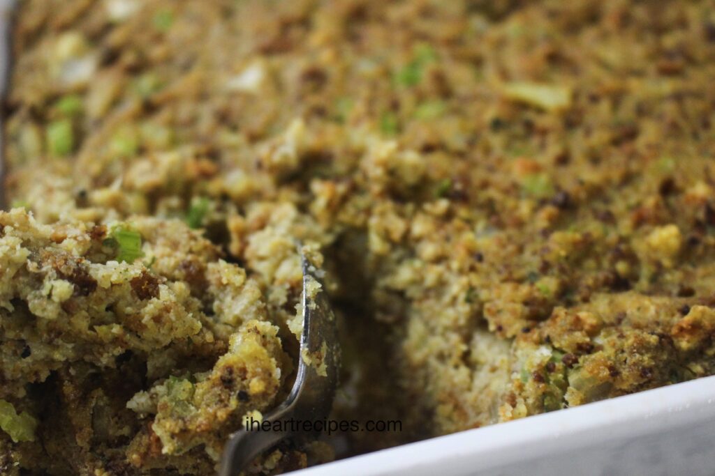 A closeup image of a casserole dish of Soul Food style cornbread dressing, with a spoon scooping a serving from the dish.