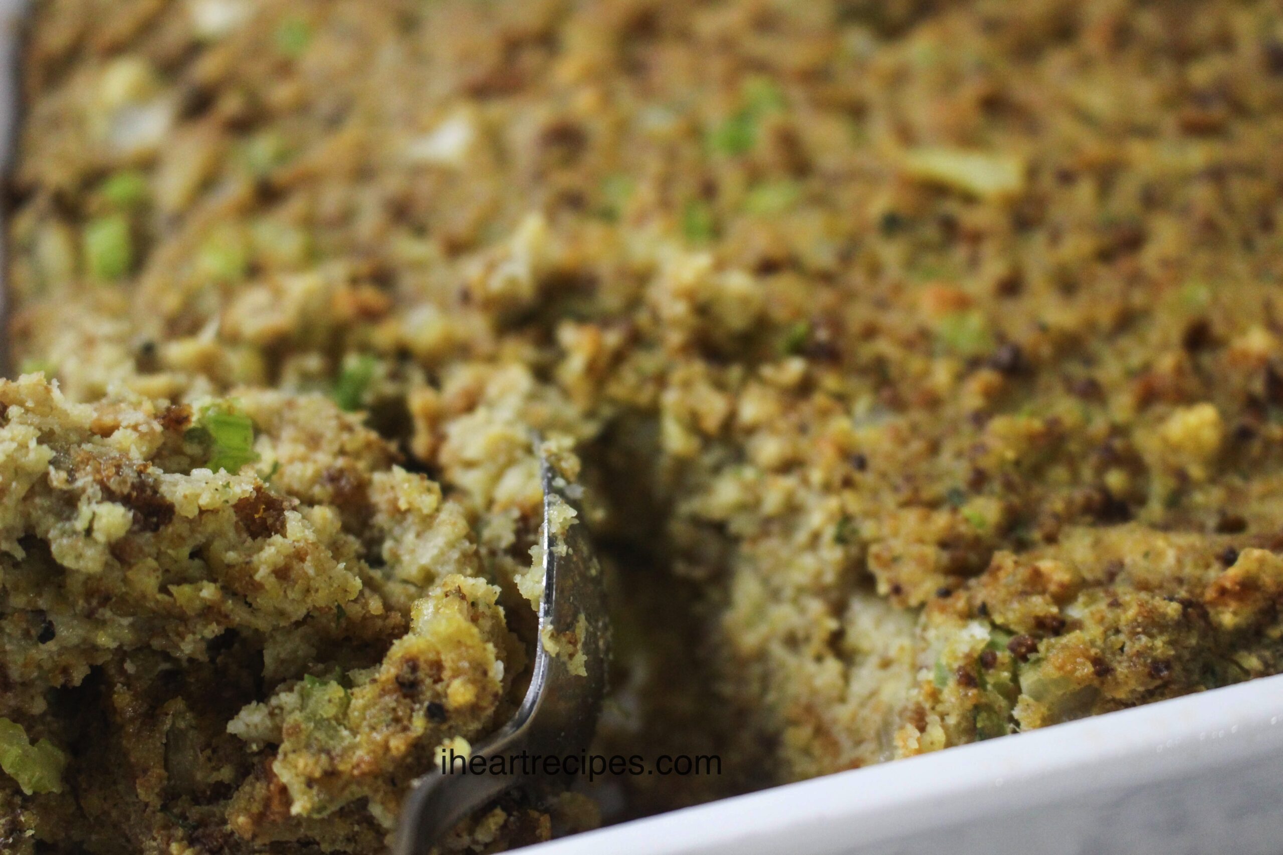 A close-up image of a savory cornbread dressing, with a metal spoon scooping up a serving.