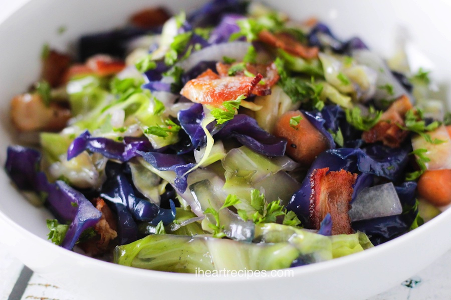 A close up of a white bowl filled with red and green cabbage, white onions, pieces of carrot and bits of crisp bacon.