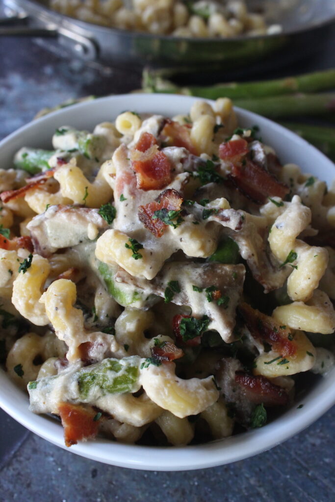 Creamy cavatappi pasta topped with bacon pieces, asparagus, and mushrooms.