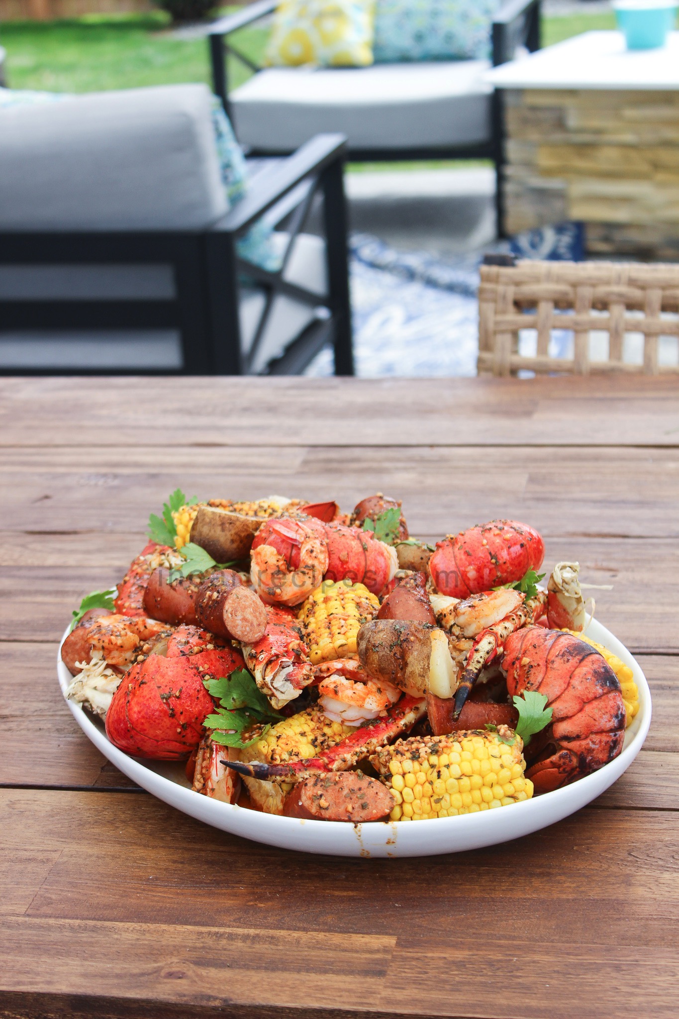 A platterful of Creole seafood boil sits on an outdoor picnic table. A variety of seafood—crab legs, lobster, and shrimp—is cooked with corn, potatoes, and Creole seasoning.