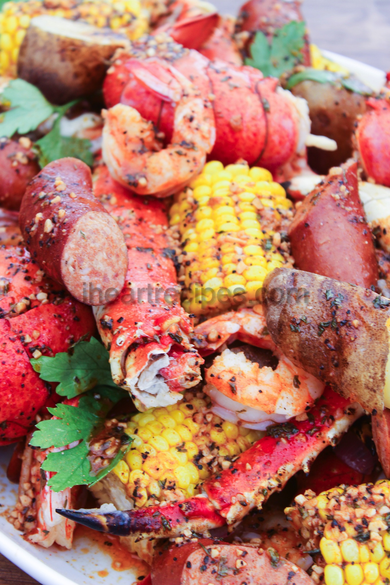 A large platter piled with flavorful andouille sausage, lobster tail, crab legs, shrimp, corn, and potatoes. The zesty seafood boil is drizzled with homemade Creole garlic butter.