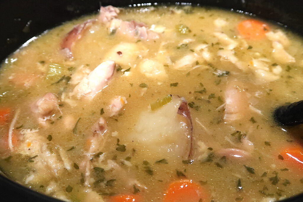 A close-up of homemade chicken stew packed with carrots, onions, potatoes, celery, chicken and seasonings all in a golden broth. 