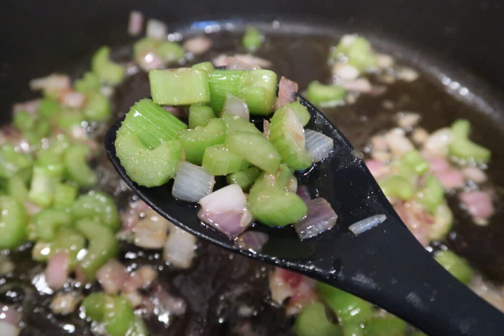 A spoonful of tender sautéed celery and onions held above a black skillet. 