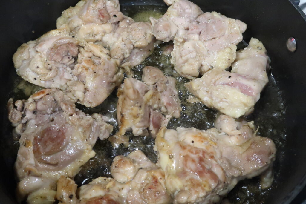 Seasoned chicken thighs sauté in a black skillet to make hearty homemade chicken stew.