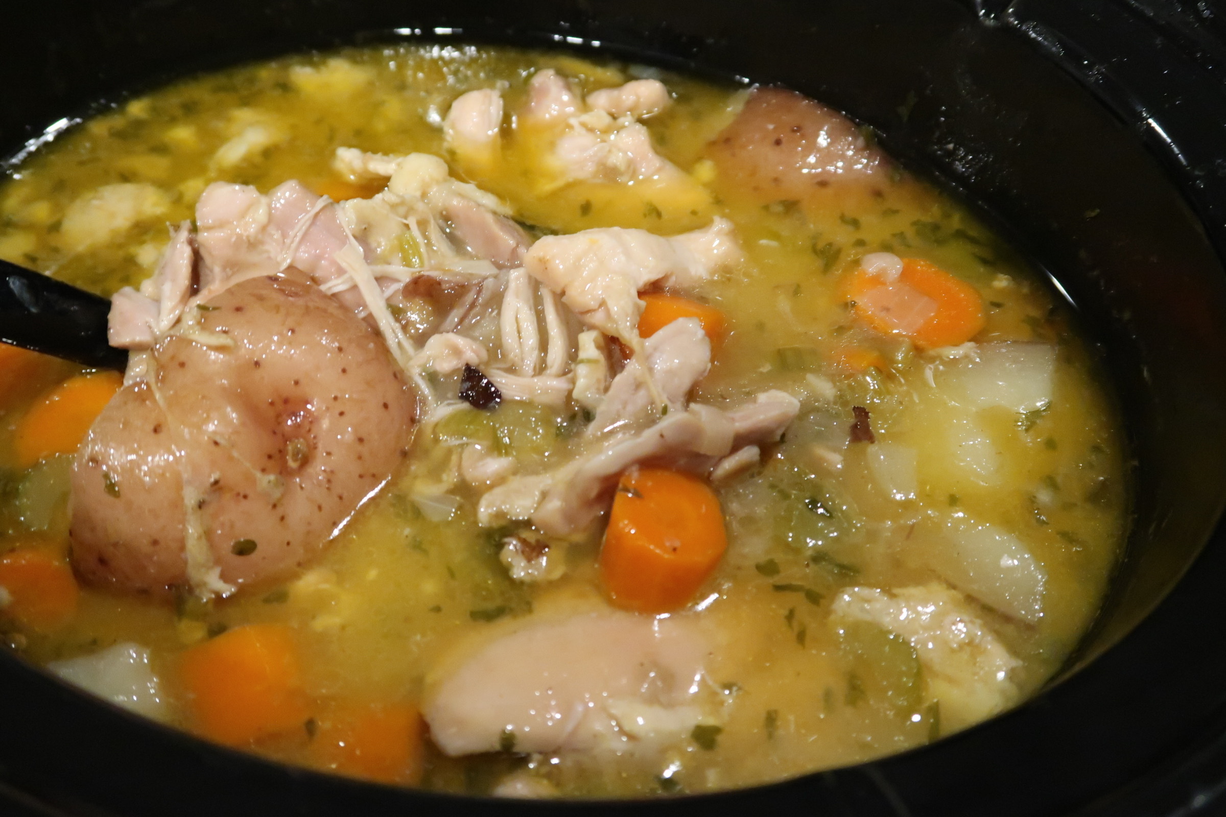 An overhead image of a full crockpot with homemade chicken stew. The stew is packed with vegetables like carrots and potatoes and tender chicken in an herby broth.