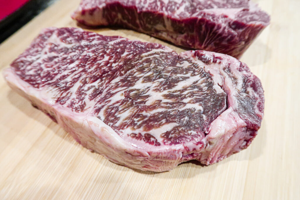 Two raw marbled wagyu steaks sit on a wooden cutting board.