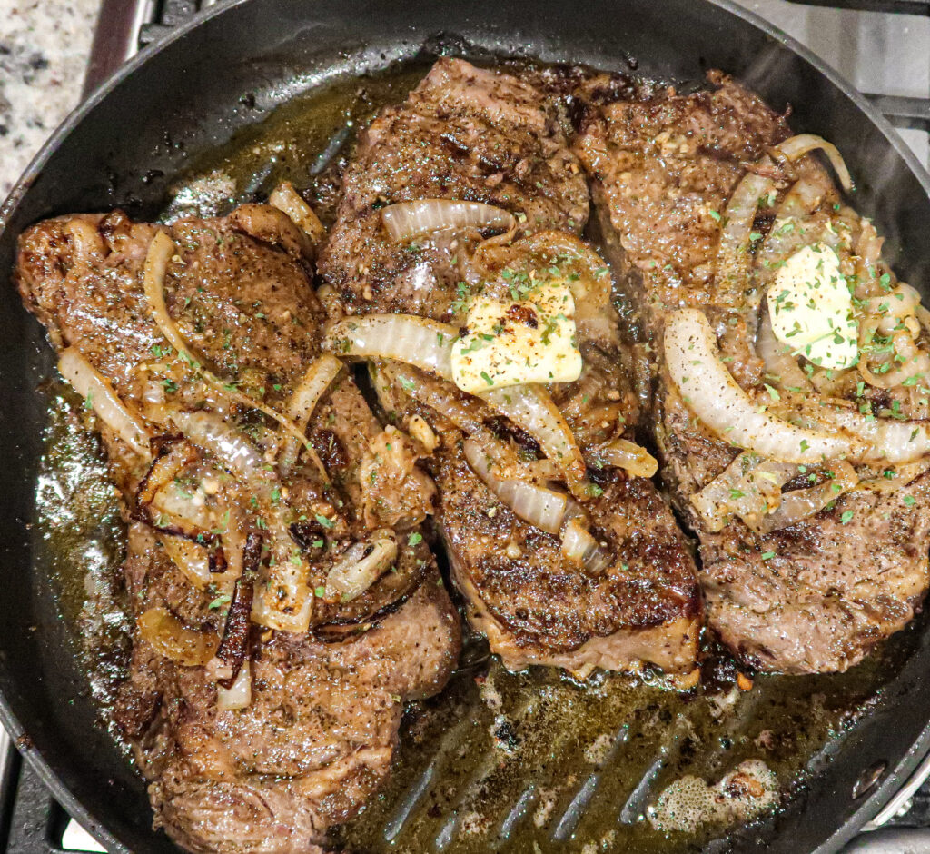 Tender wagyu steak topped with onions, parsley, and butter in a grill pan.