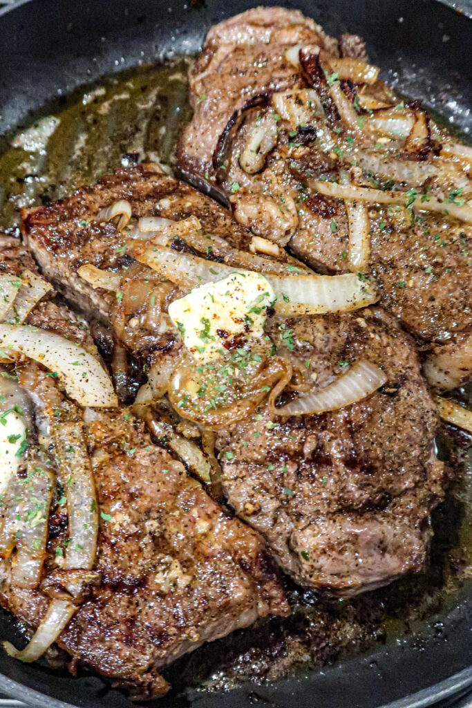 Tender, juicy wagyu steaks covered with steak seasoning, onions, parsley flakes, and butter cook in a grill pan.