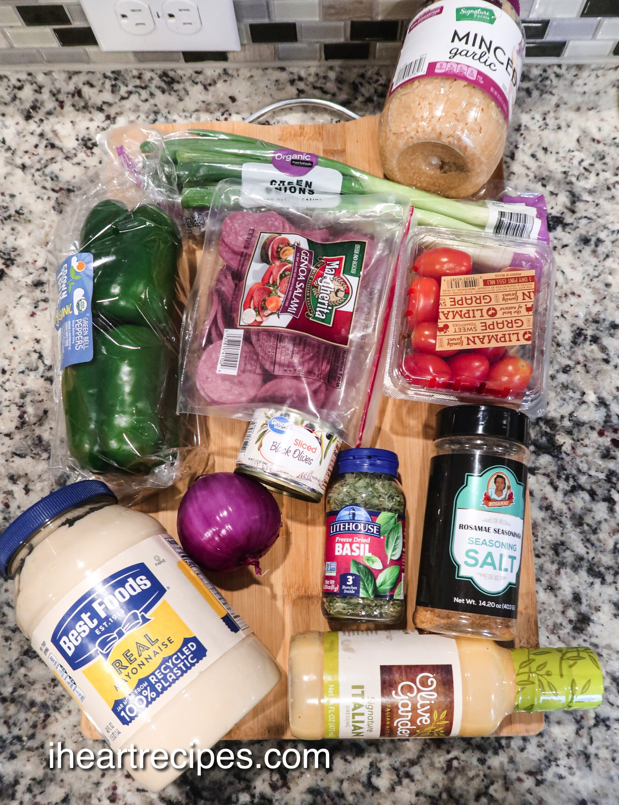 An overhead image of all the ingredients needed to make Italian pasta salad, laid out on a wooden cutting board. 