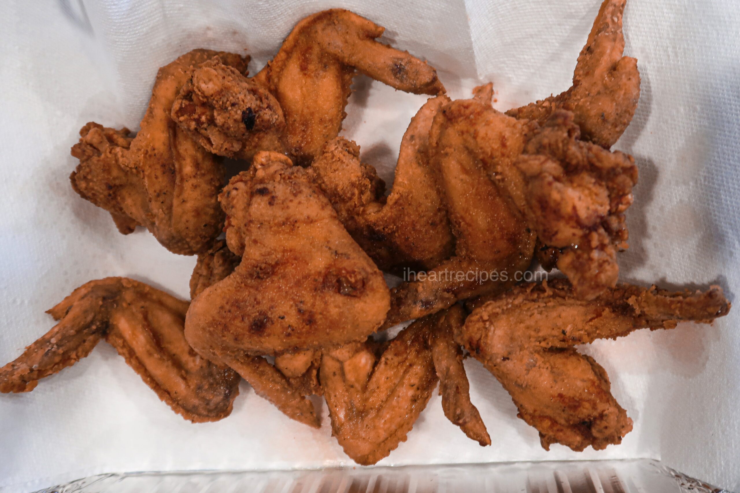 An overhead image of crispy, golden brown skillet fried chicken wings resting on white paper towels.