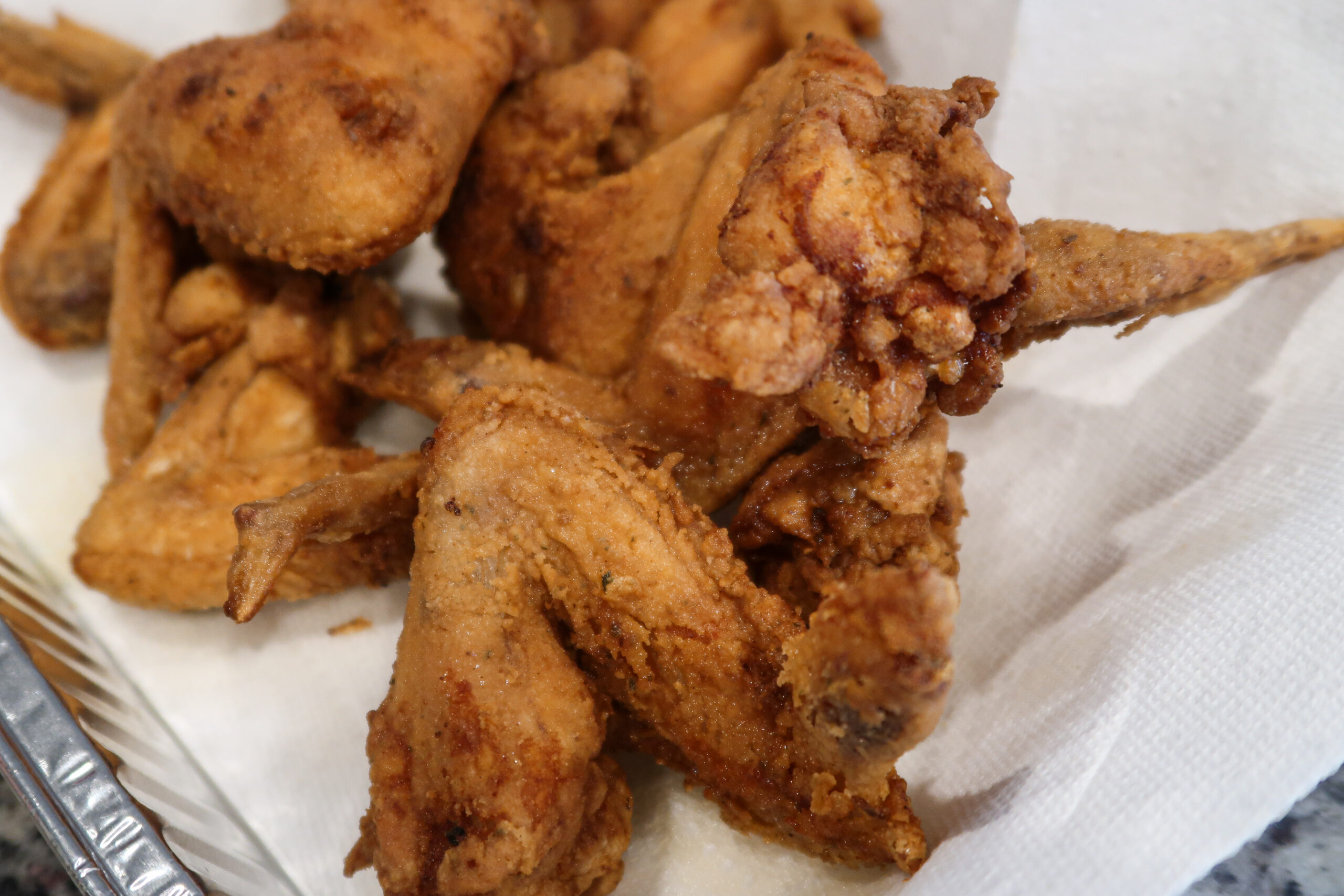 A closeup of skillet-fried chicken wings on a white paper towel. The chicken wings are breaded and fried to a crisp golden brown.