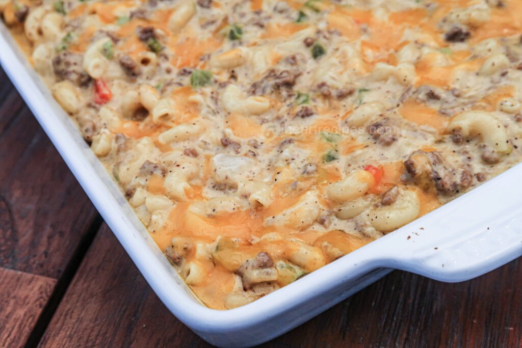 Creamy homemade Cheeseburger Hamburger Helper, made with macaroni, hamburger, shredded cheese, and fresh vegetables, fills a white bake dish set on a wooden table.