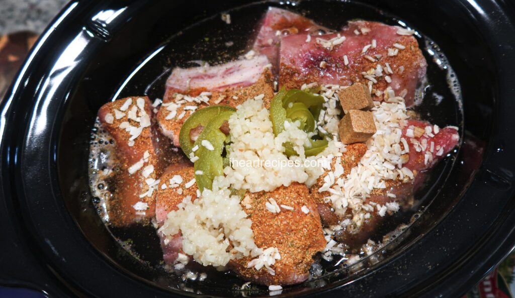 All the ingredients needed to make delicious southern style pigs feet - pigs feet, onions and garlic, broth, and jalapeno peppers - tossed in a slow cooker.